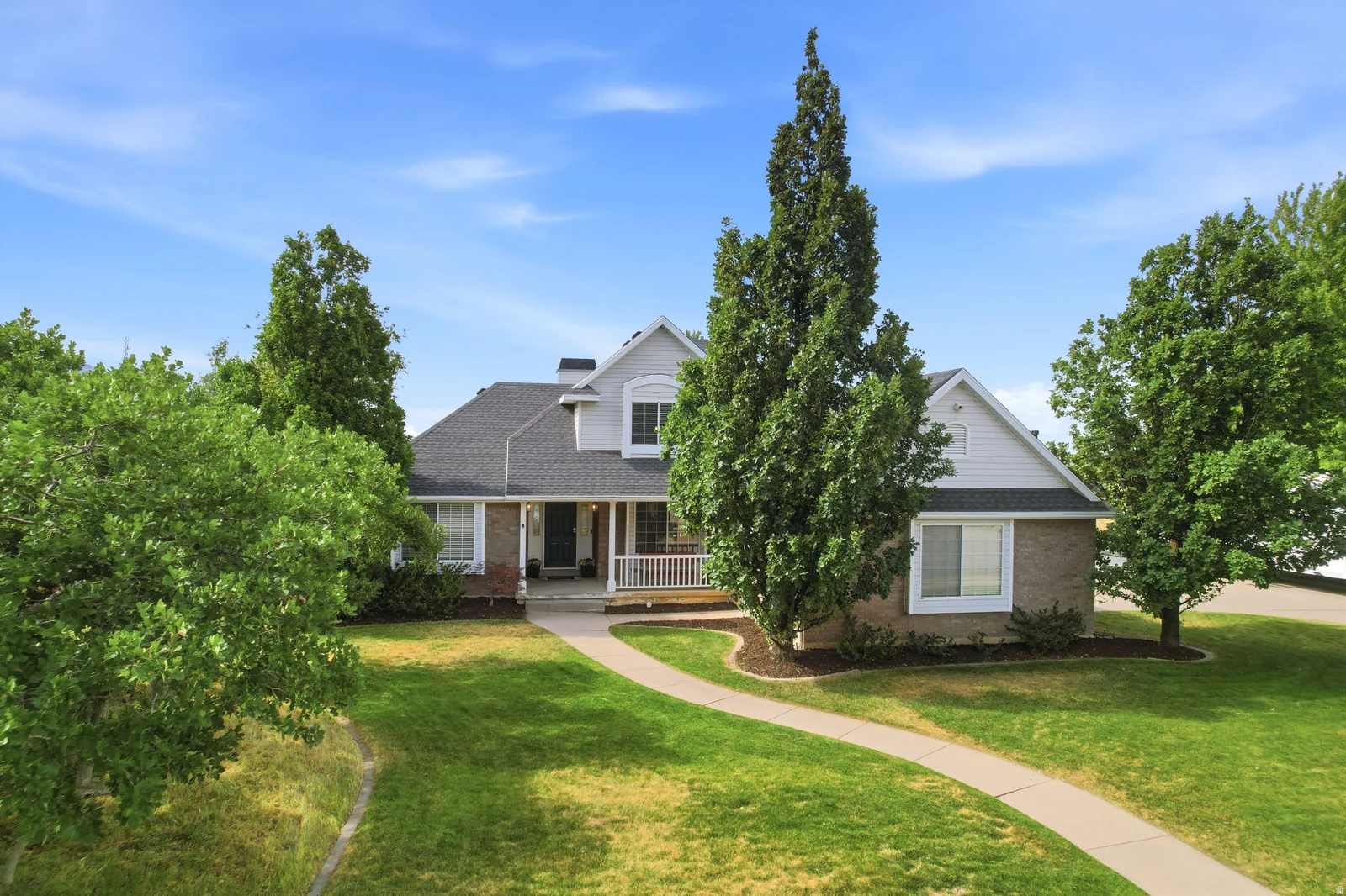 Traditional-style residence featuring a prominent front porch with white railings, a dark shingled roof, and a combination of light-colored siding and brick accents
